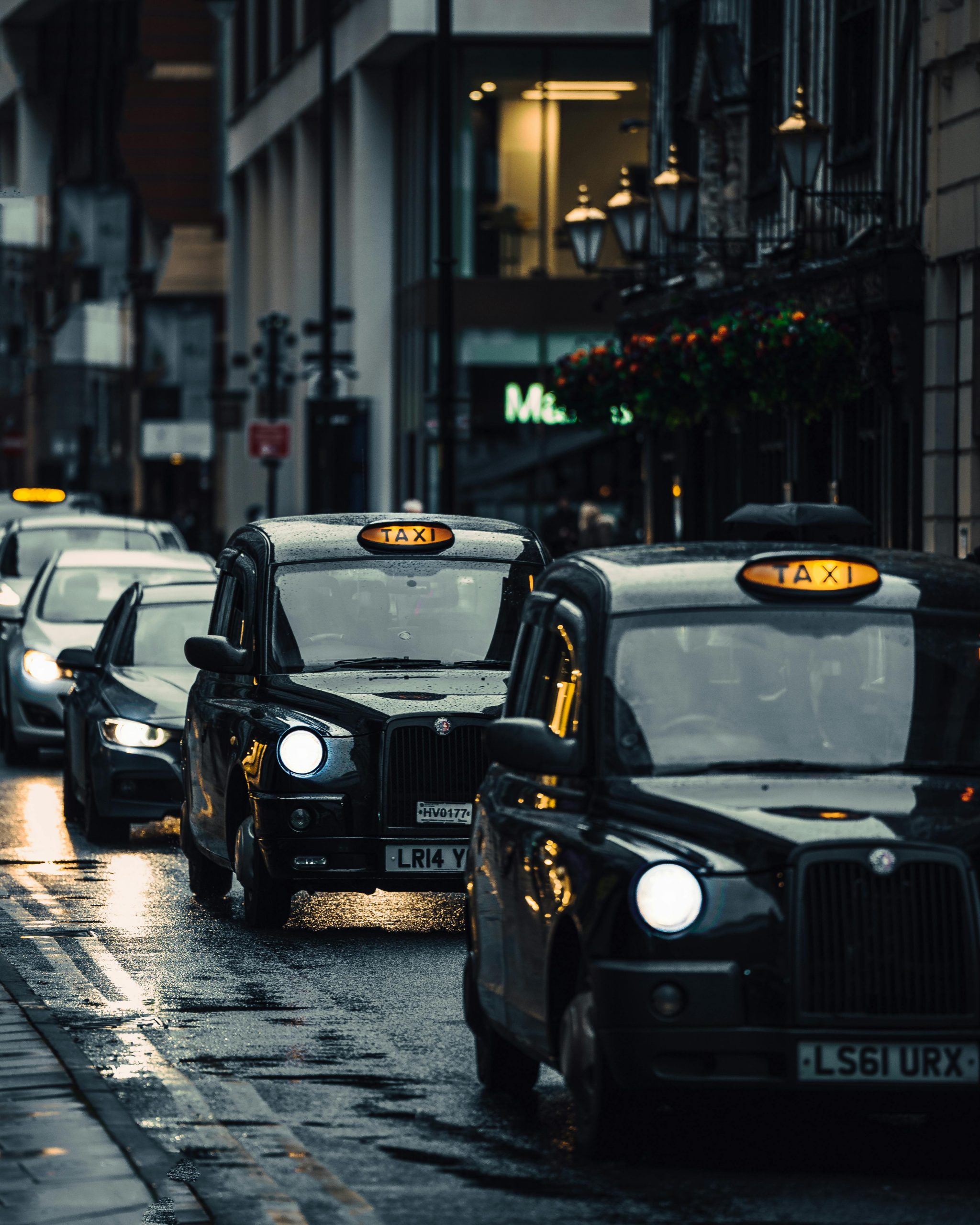 Classic London taxis navigating wet streets in an atmospheric cityscape.
