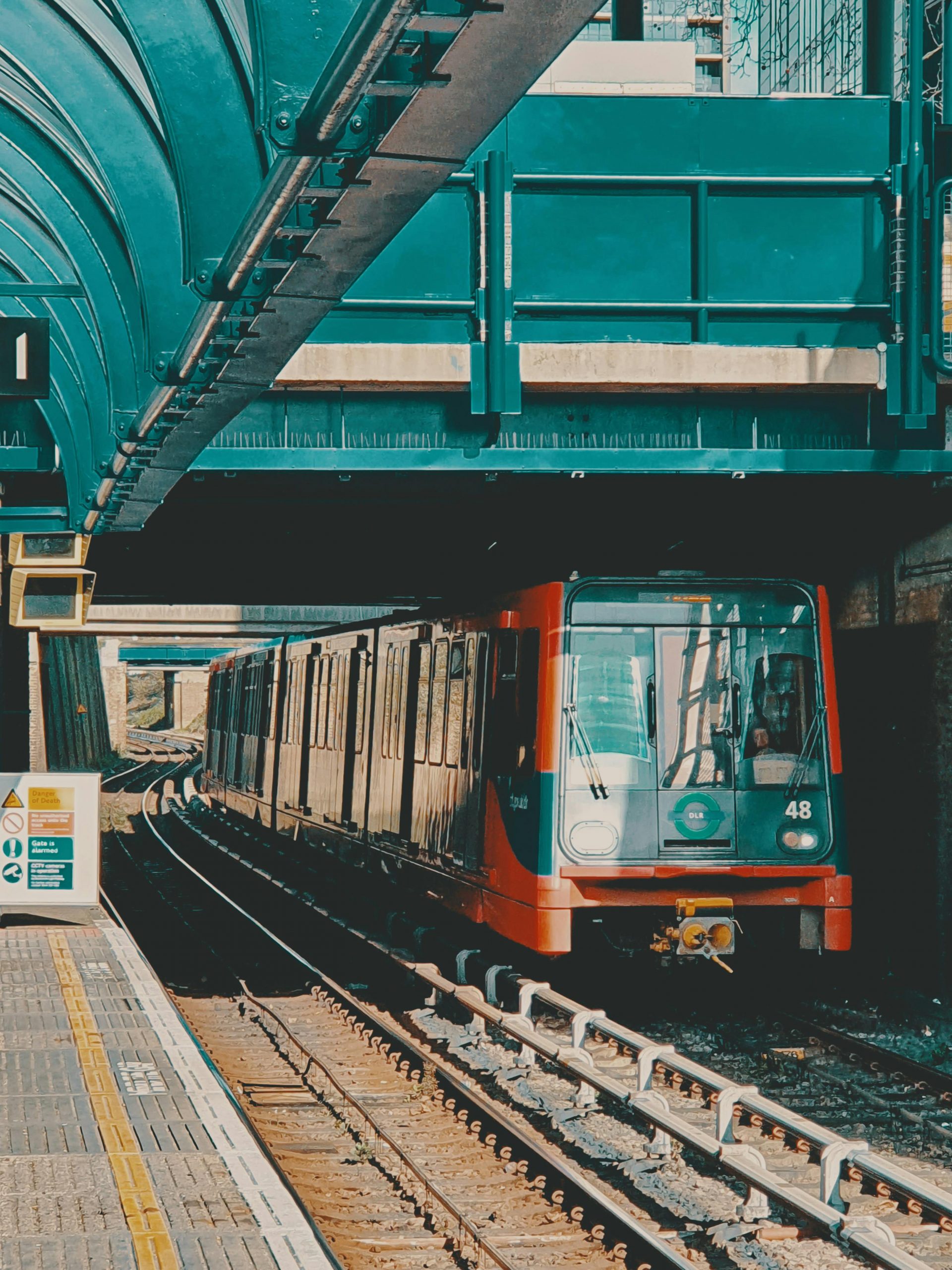 A Docklands Light Railway train arriving at a London station on a bright summer day.