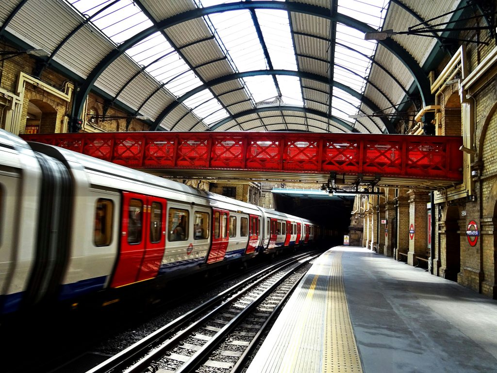 A vibrant red bridge contrasts with a sleek train at a historic railway station, showcasing travel and architecture.