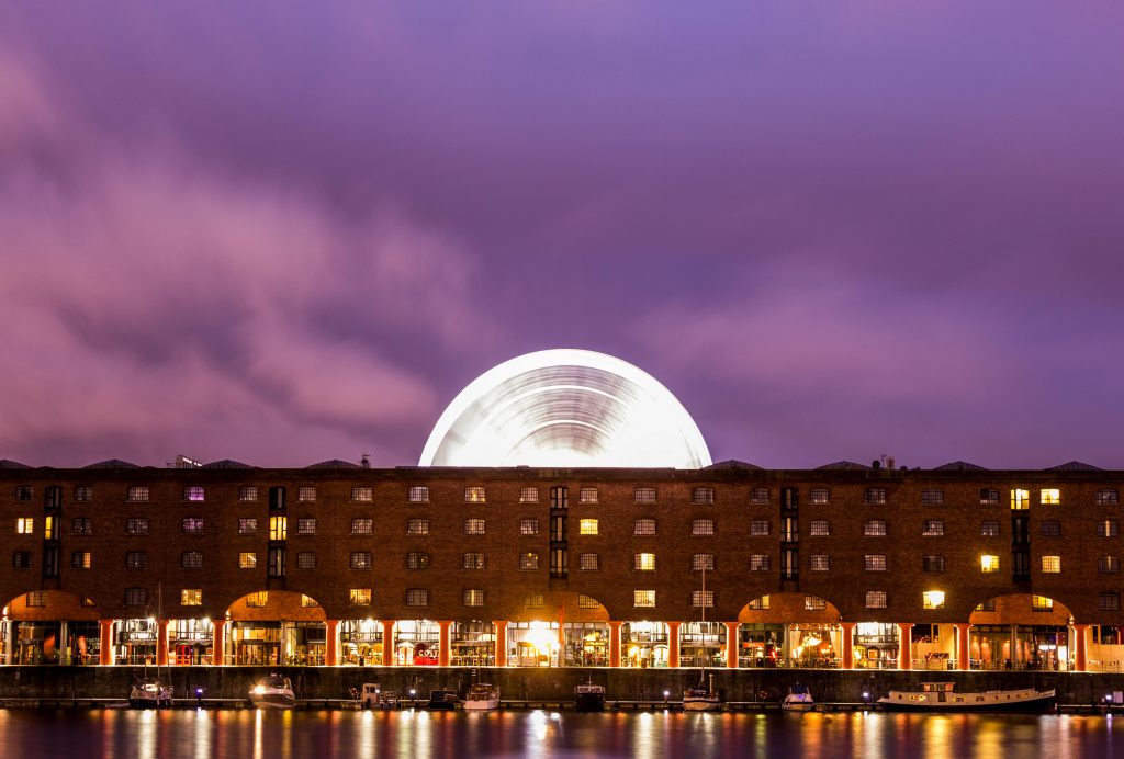 Illuminated Albert Dock with ferris wheel reflection at night in Liverpool, UK.